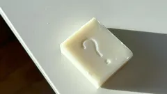 Bílá kostka se znakem otazníku na bílém povrchu, makro detail.