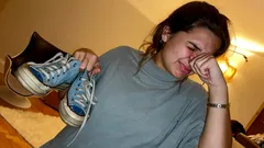 Žena drží boty a dává si ruku k nosu, výraz znechucení zápachem bot.